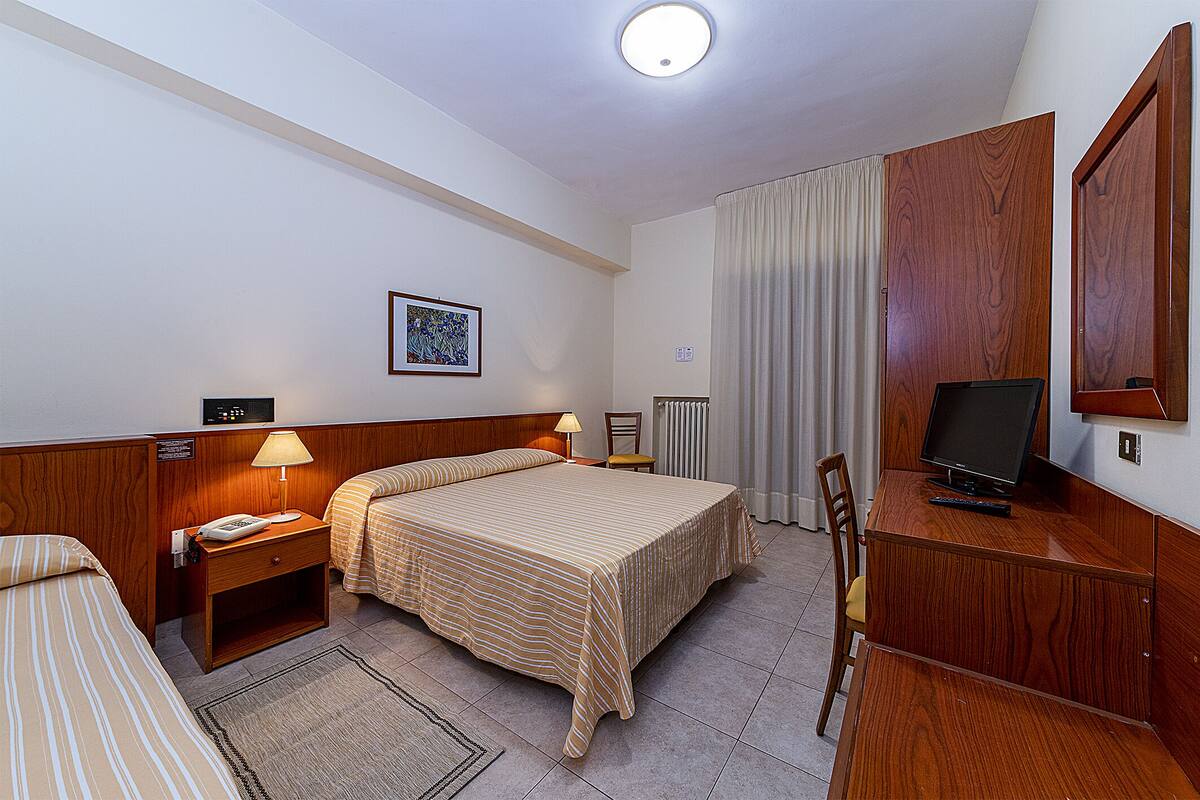 A hotel room with a bed, a desk with a computer, a chair, a lamp, and a television.