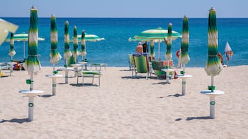 A beach with rows of green and white umbrellas, white lounge chairs, and a clear view of the ocean.