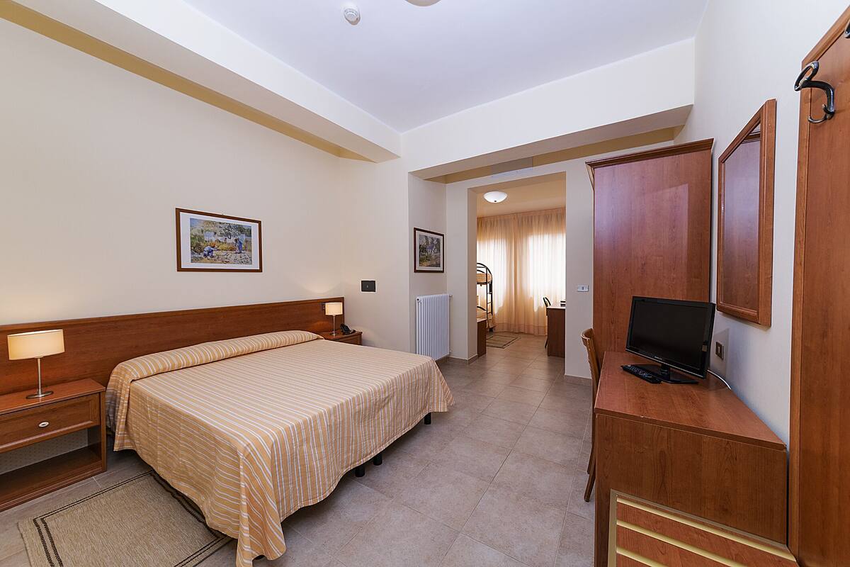 A hotel room with a bed, bedside table, lamp, desk with a computer, and a mirror.