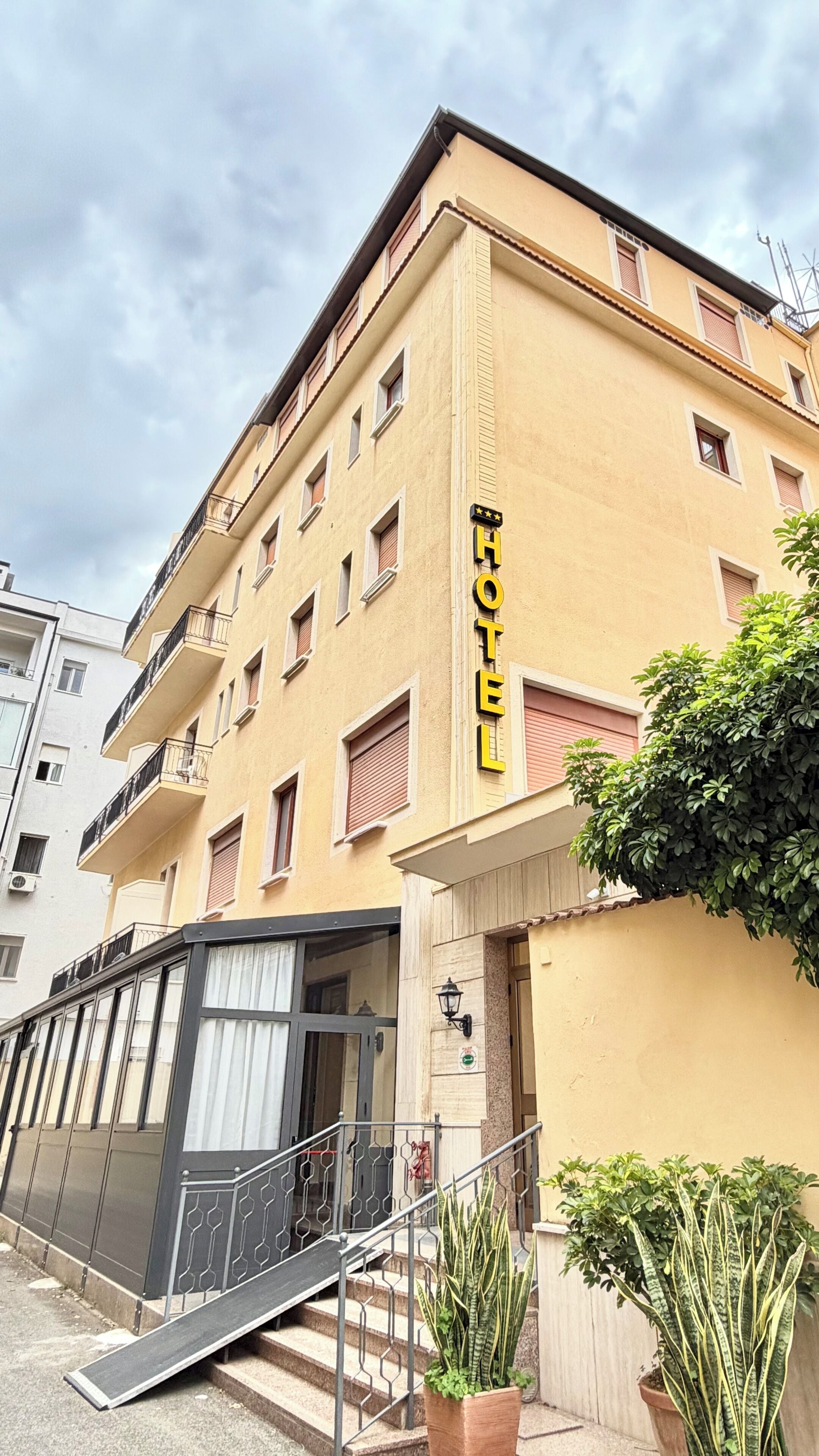 A hotel with a yellow facade, a staircase leading to the entrance, and a sign indicating it is a 3-star establishment.