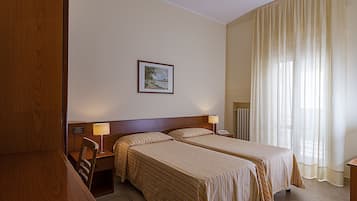Une chambre d’hôtel avec deux lits, un bureau, une chaise, un tableau encadré au mur et une fenêtre avec des rideaux.