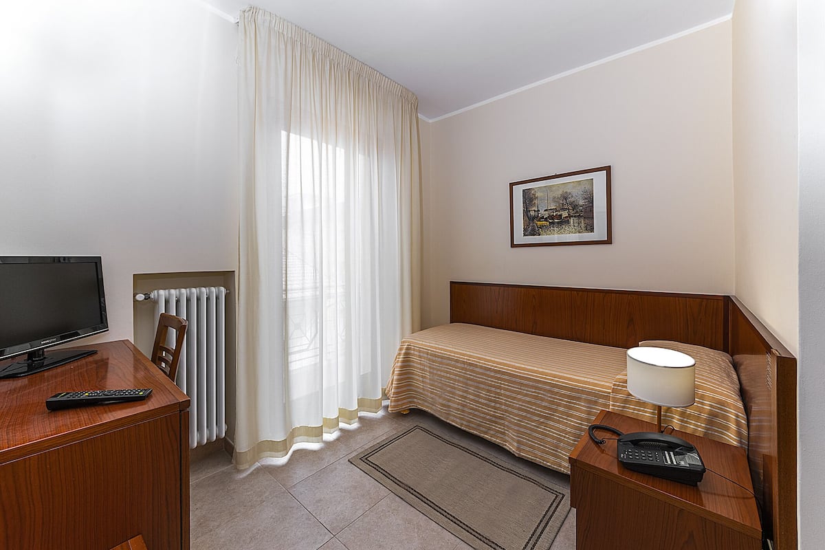 A hotel room with a bed, a desk with a TV, a chair, a lamp, and a framed picture on the wall.