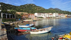 Una località costiera con barche ormeggiate al molo, edifici con balconi e montagne sullo sfondo.
