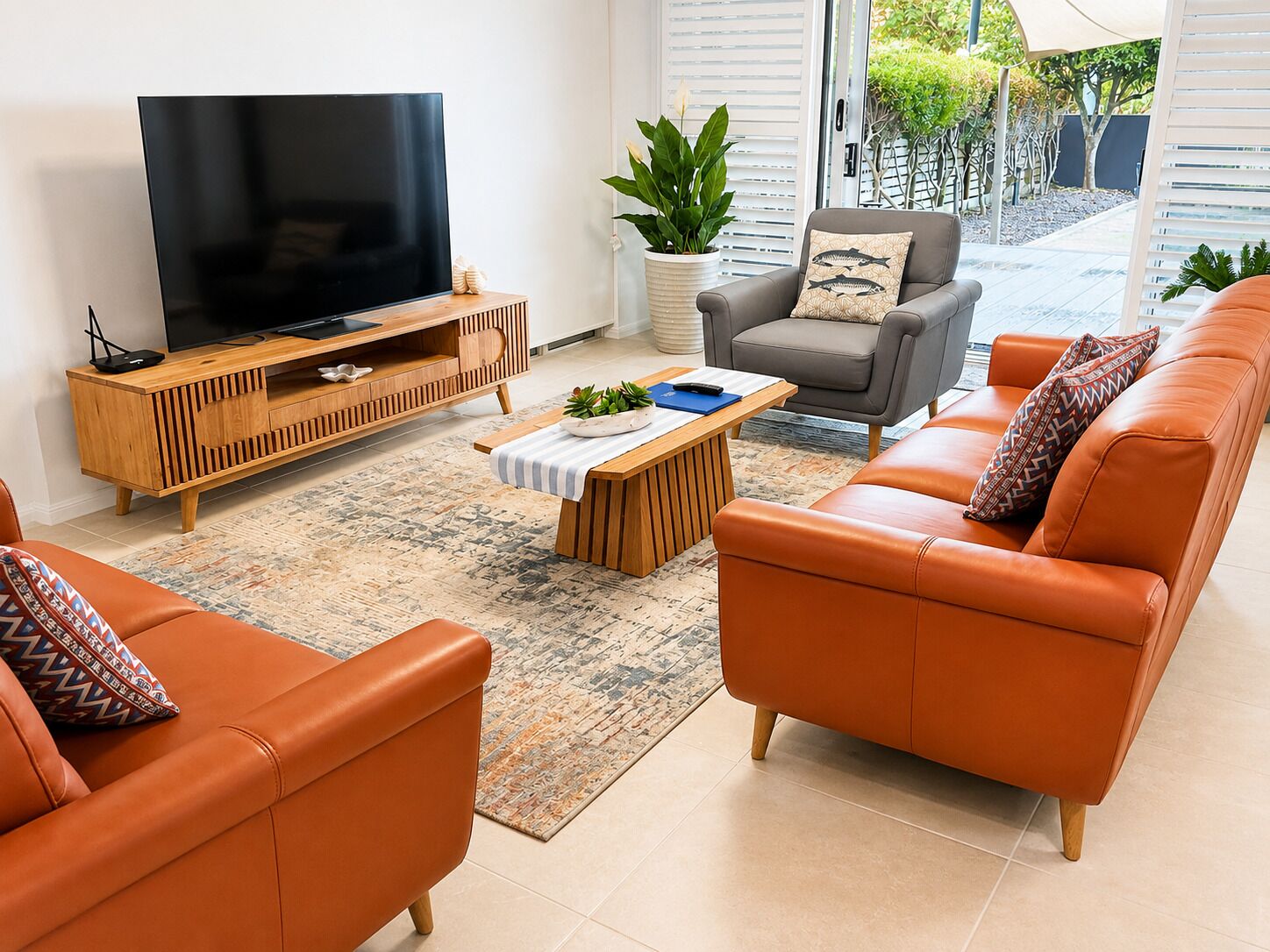 Ein modernes Wohnzimmer mit einem Flachbildfernseher, einer Holz-Unterhaltungsecke, einem grauen Sessel, einem orangefarbenen Sofa und einem gemusterten Teppich.