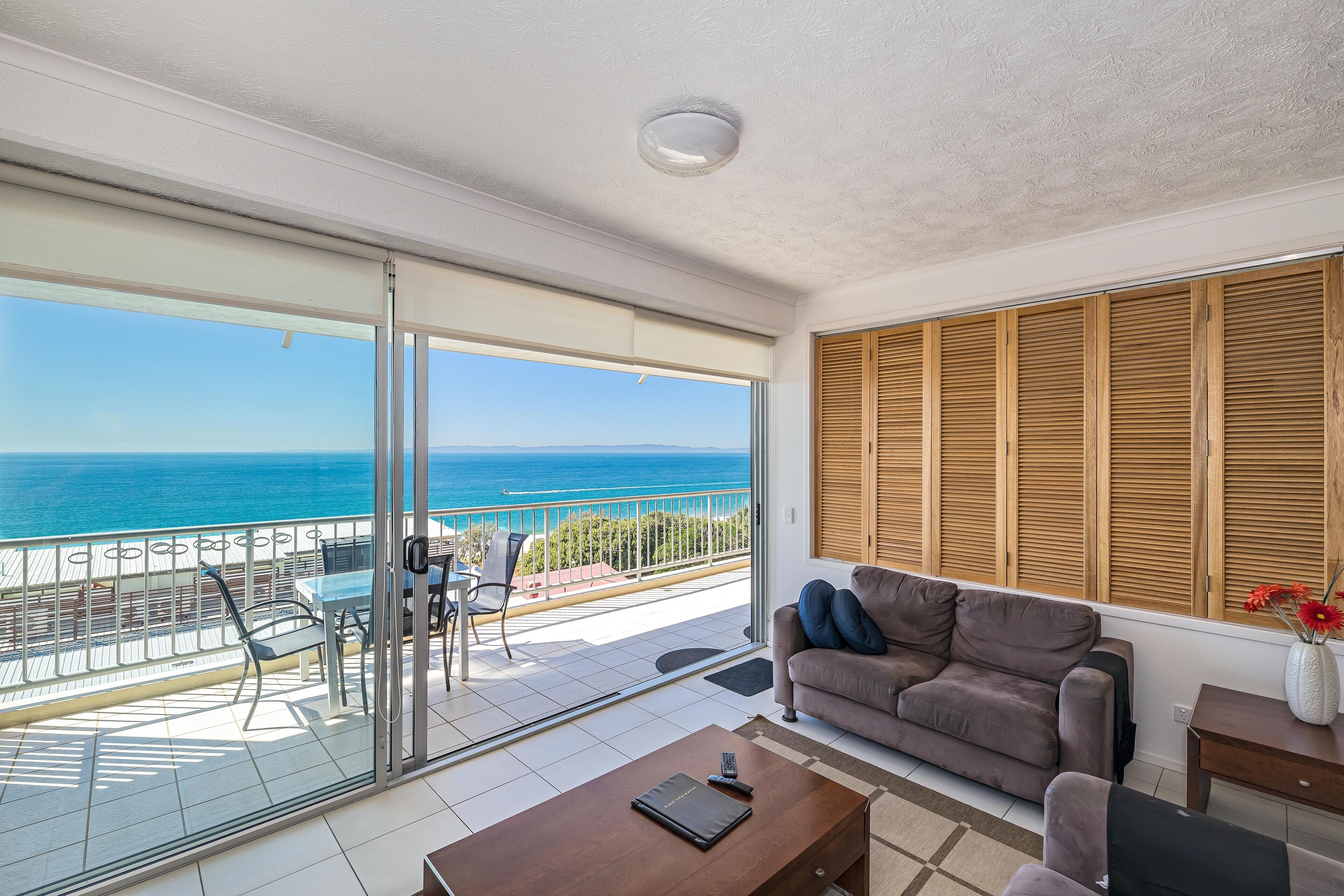 A balcony with a view of the sea, a sofa, a coffee table, and a dining area with chairs.