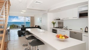 A modern kitchen with a large island, bar stools, and a view of the ocean. - On the Beach Resort Bribie Island (Woorim)