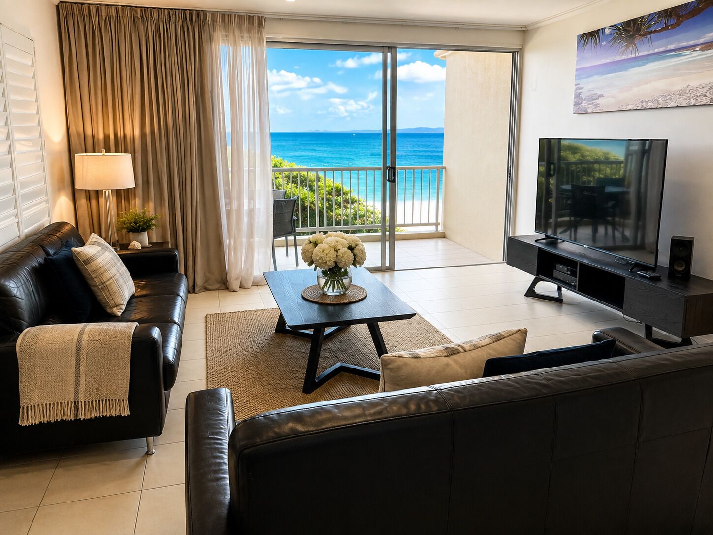 A living room with a sofa, a coffee table with flowers, a TV, and a view of the ocean.