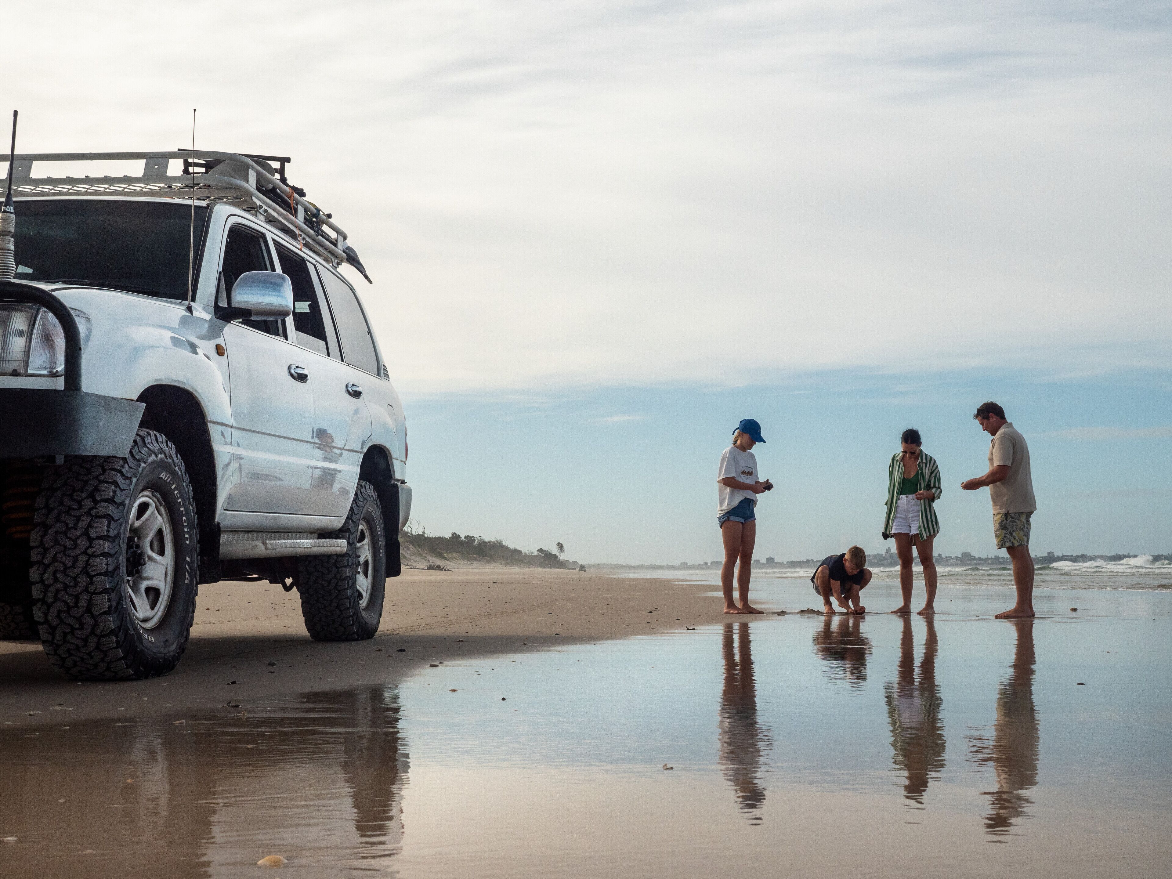 Un SUV blanco estacionado en una playa arenosa bajo un cielo despejado.