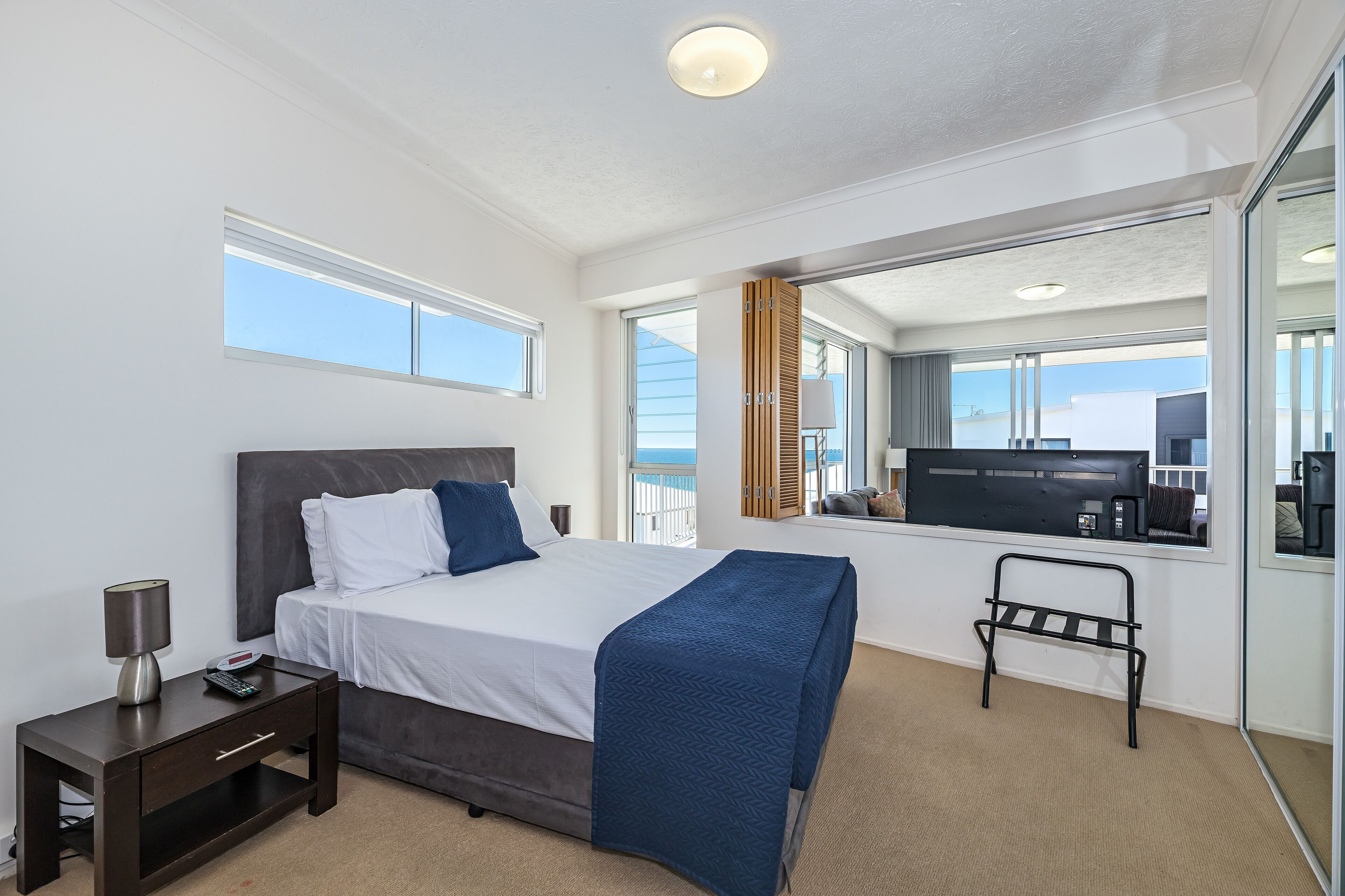 Une chambre d’hôtel moderne dotée d’un grand lit, d’une table de chevet, d’un petit bureau, d’une chaise et offrant une vue sur la mer grâce à une grande fenêtre.