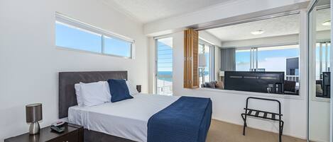 Une chambre d’hôtel moderne dotée d’un grand lit, d’une table de chevet, d’un petit bureau, d’une chaise et offrant une vue sur la mer grâce à une grande fenêtre.