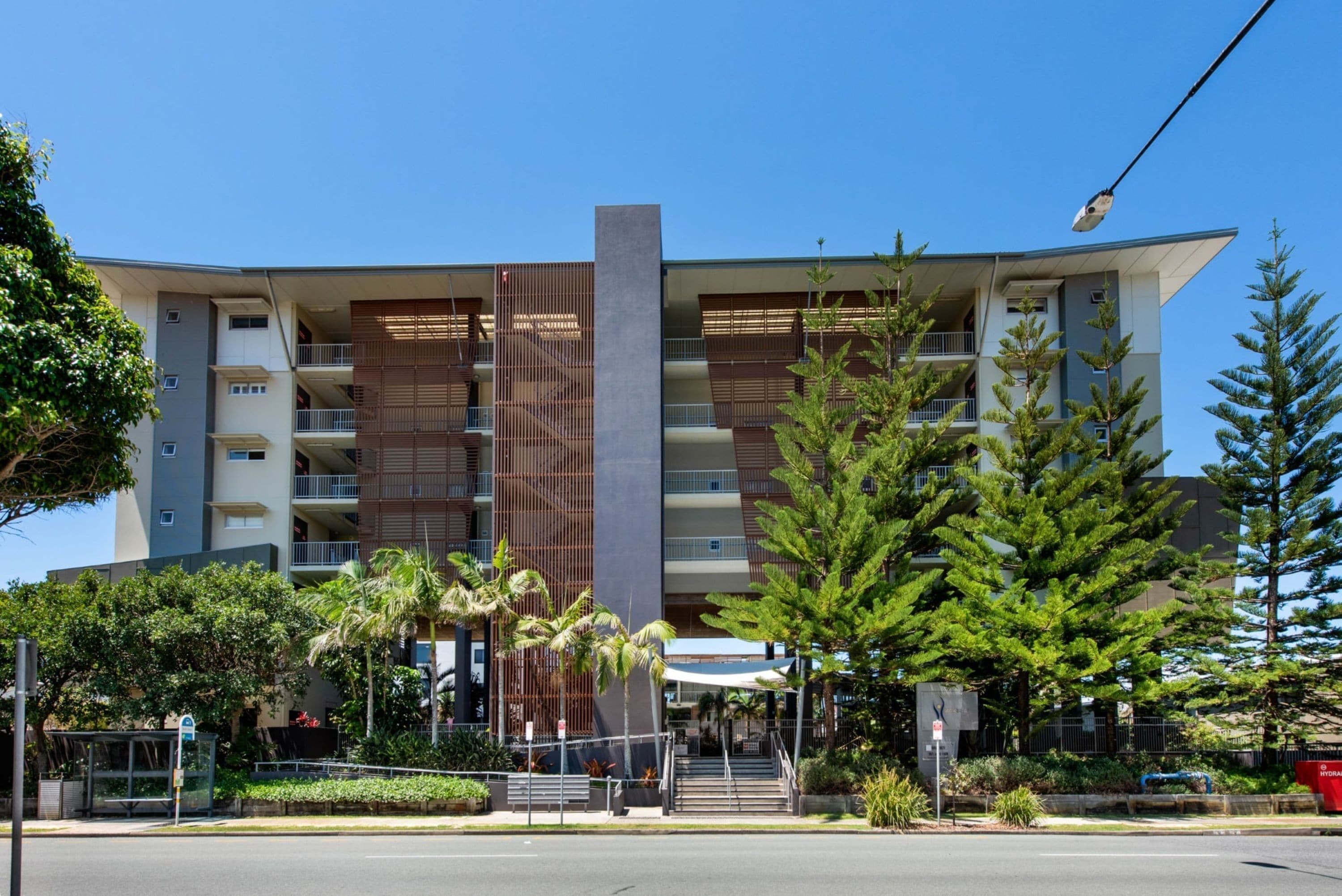 Un edificio moderno de varios pisos con balcones, una estructura vertical central y zonas verdes circundantes.