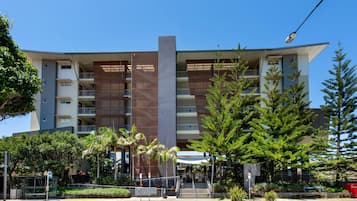 Un edificio moderno de varios pisos con balcones, una estructura vertical central y zonas verdes circundantes.