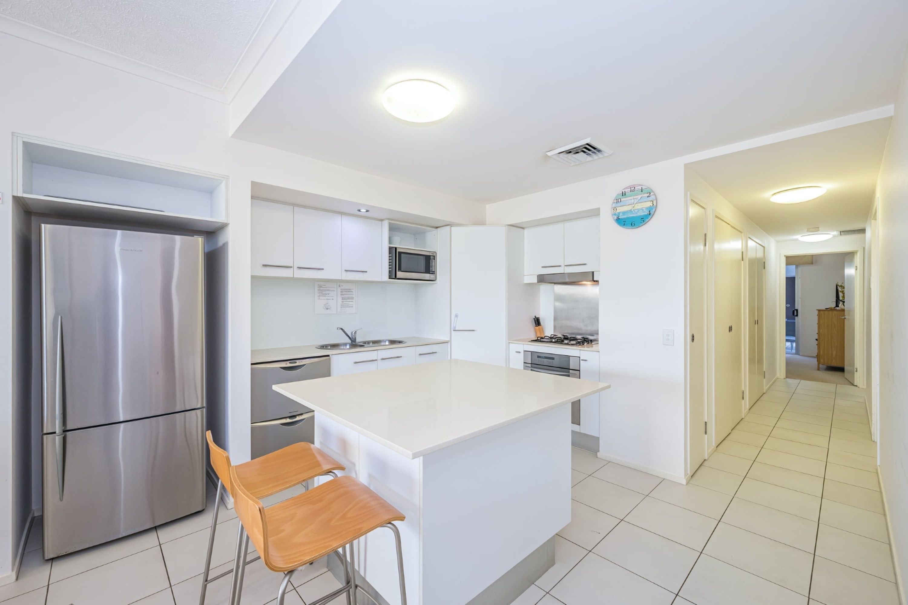 Een moderne keuken met witte kasten, roestvrijstalen apparatuur en een centraal eiland met barstoelen.