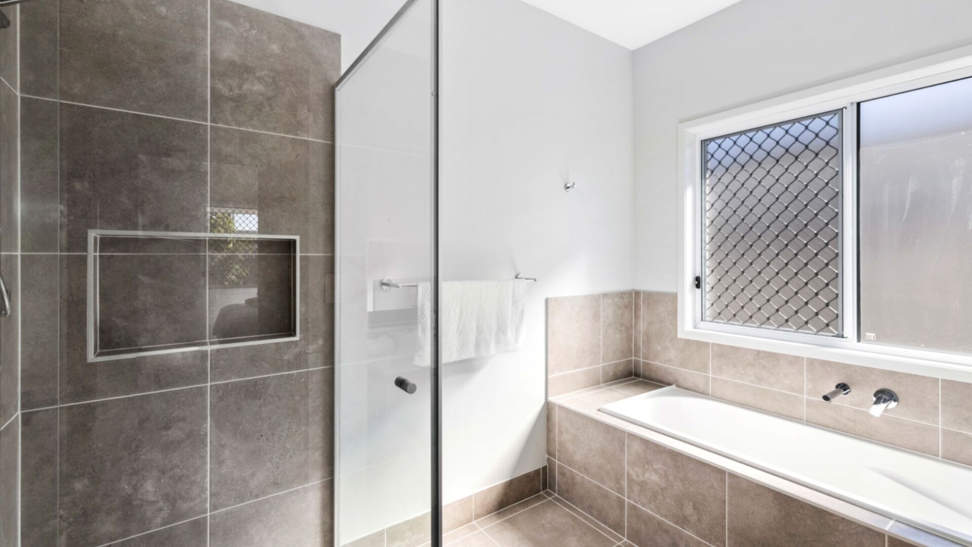 Une salle de bain moderne avec une douche à l’italienne en verre, une grande baignoire et une fenêtre dotée d’un moustiquaire métallique.