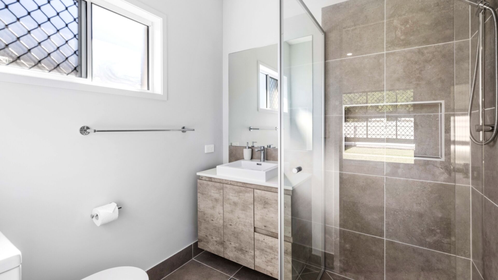 Ein modernes Badezimmer mit Duschkabine aus Glas, einem weißen Waschbecken und einem Holz-Badmöbel