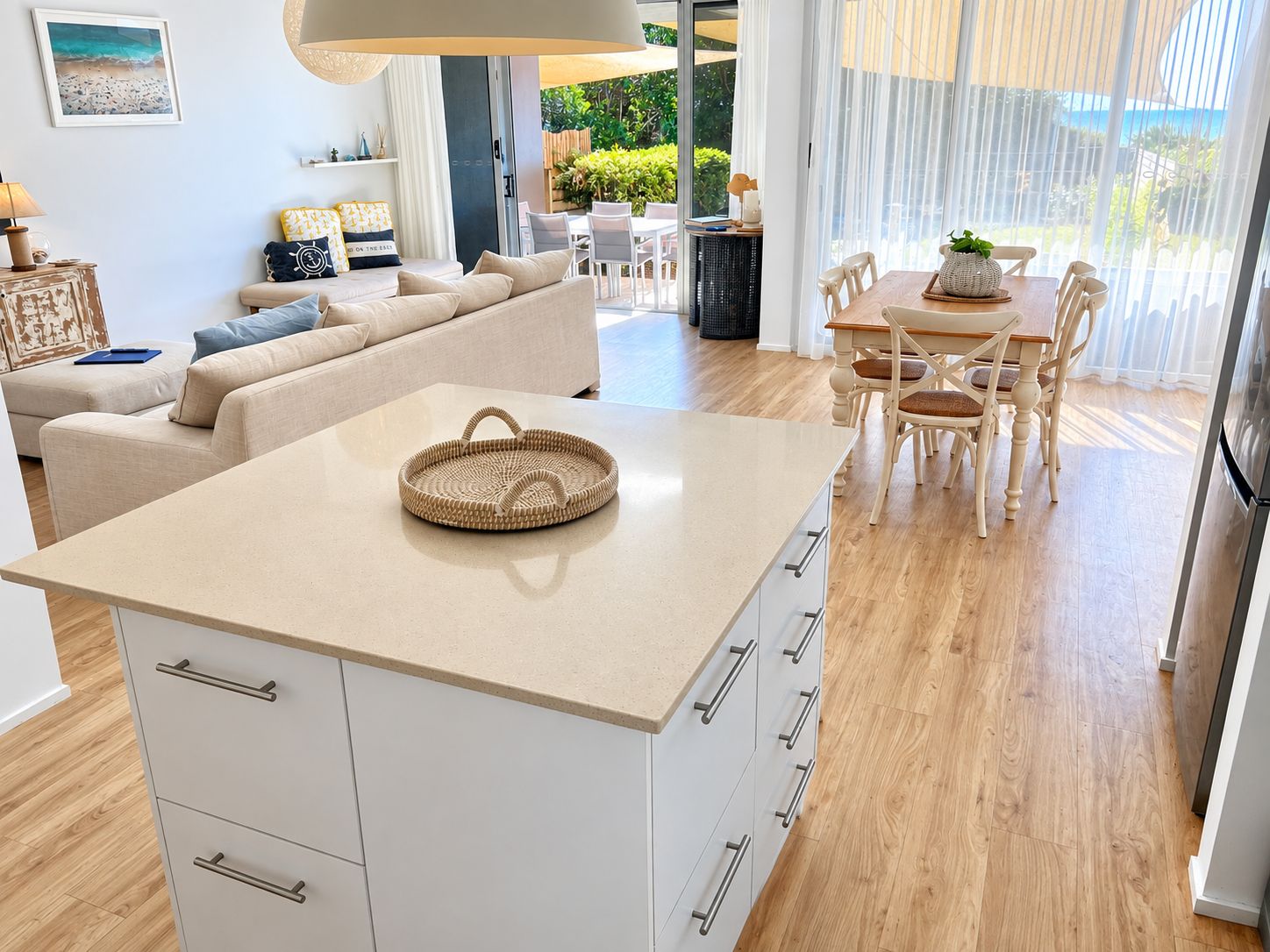 A modern living room with a sofa, a dining table with chairs, a kitchen area with a countertop and cabinets, and a view of the outdoors.
