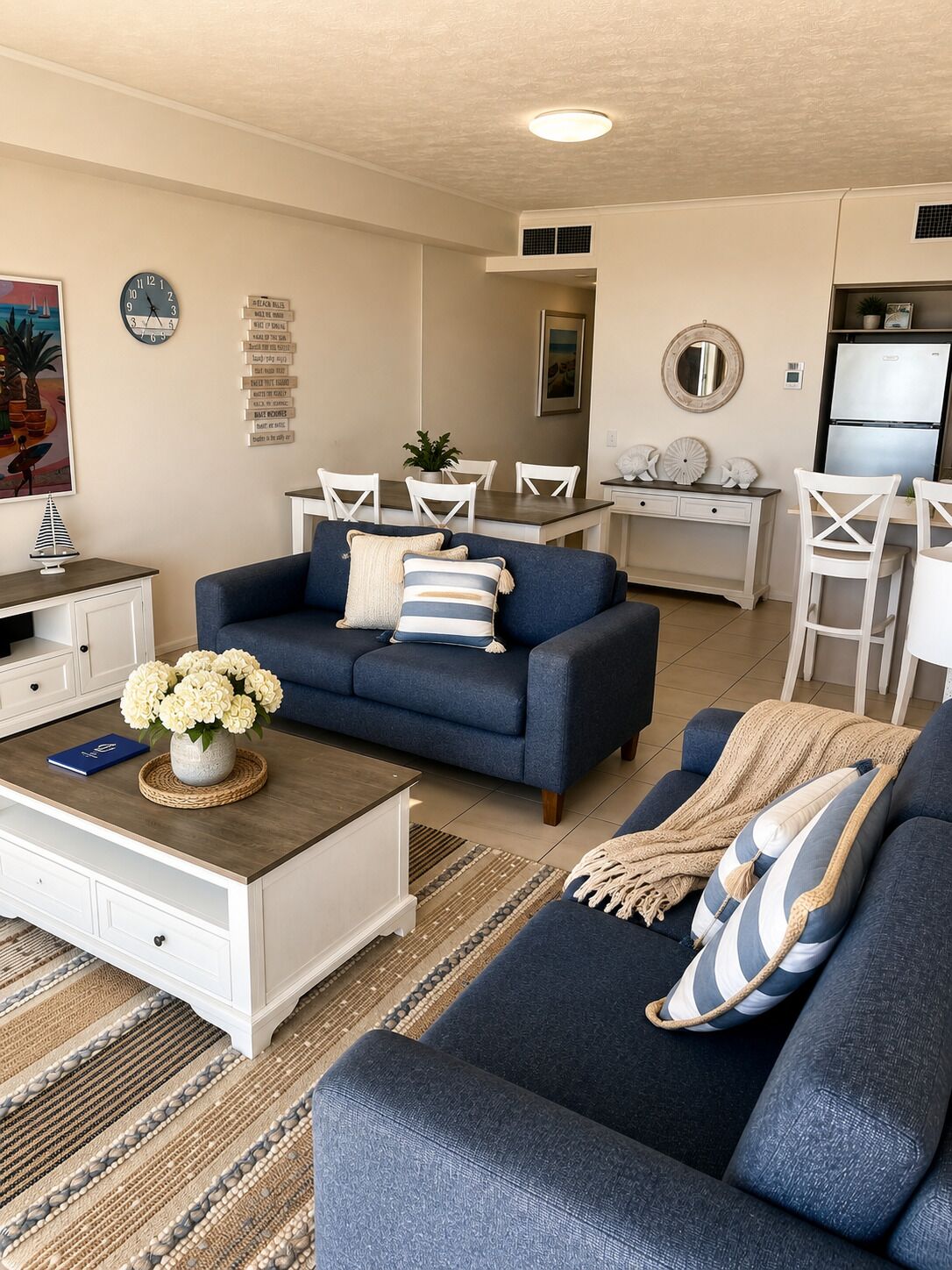 Un salon moderne avec un canapé bleu, une table basse ornée d’un vase de fleurs et un coin repas avec des chaises blanches et une table.