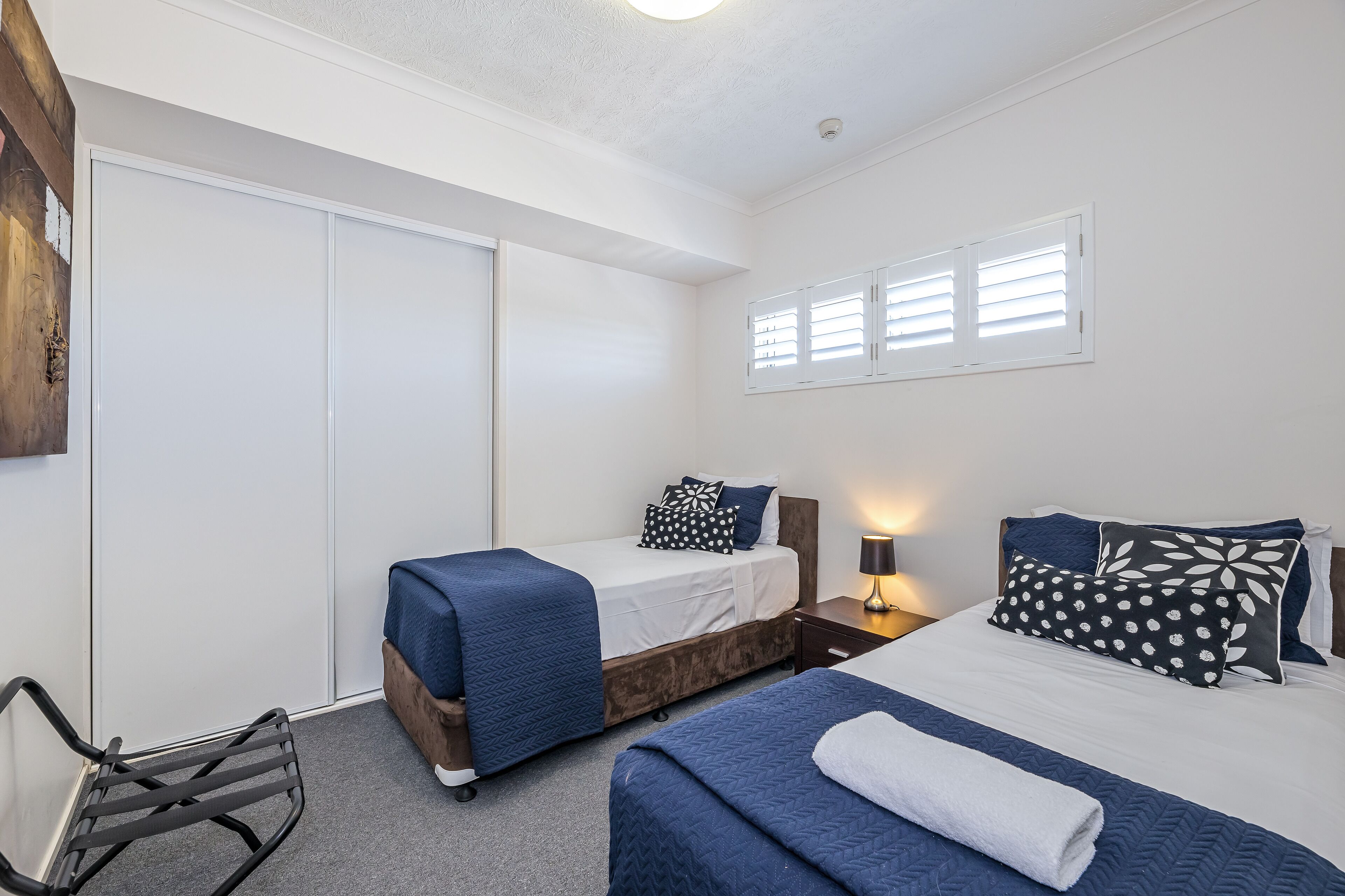 A bedroom with two beds, a chair, a wardrobe, and a window with blinds.