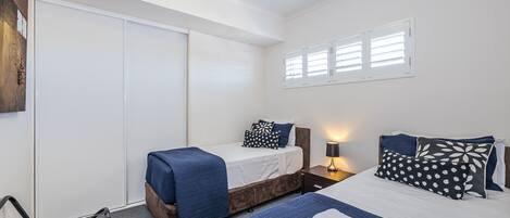 A bedroom with two beds, a chair, a wardrobe, and a window with blinds.