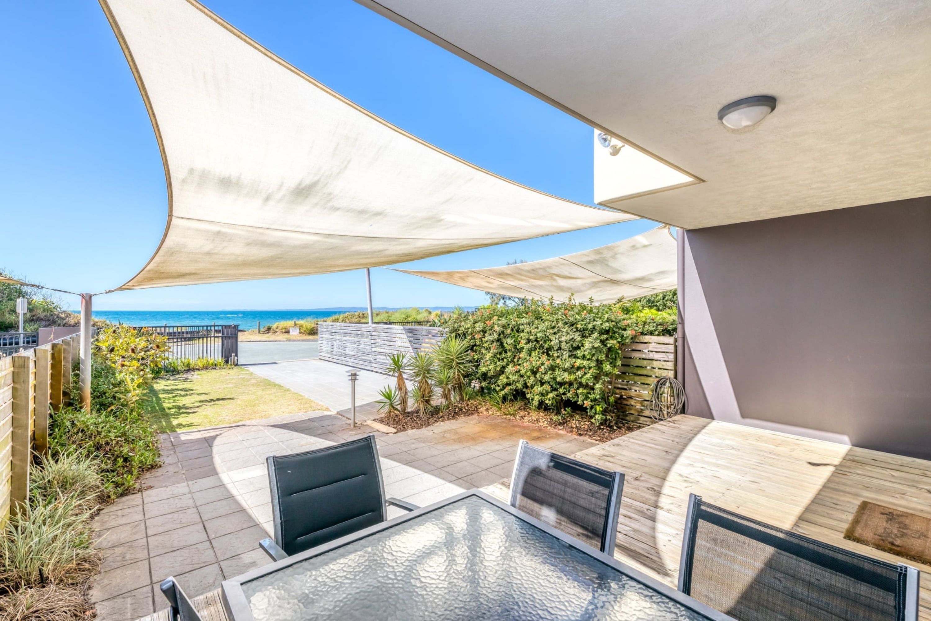 Une terrasse avec une table et des chaises en verre, un auvent blanc et une vue sur l’océan.