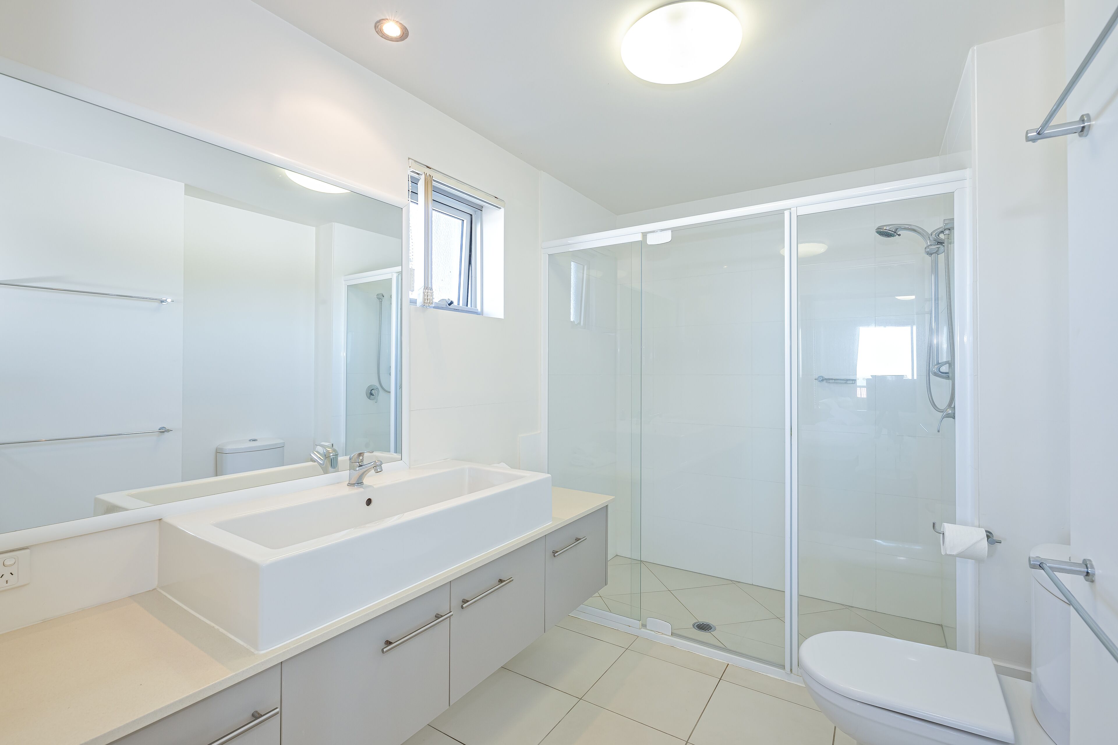 Ein modernes Badezimmer mit einem großen, weißen Waschbecken, einer Glaskabine für die Dusche und einer Toilette.