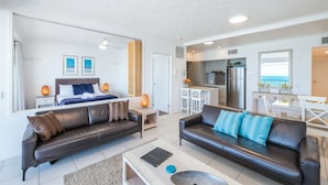 A modern living room with a sofa, a coffee table, and a dining area. - On the Beach Resort Bribie Island (Woorim)