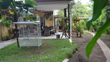 A covered patio area with outdoor furniture, a birdcage, and various potted plants.