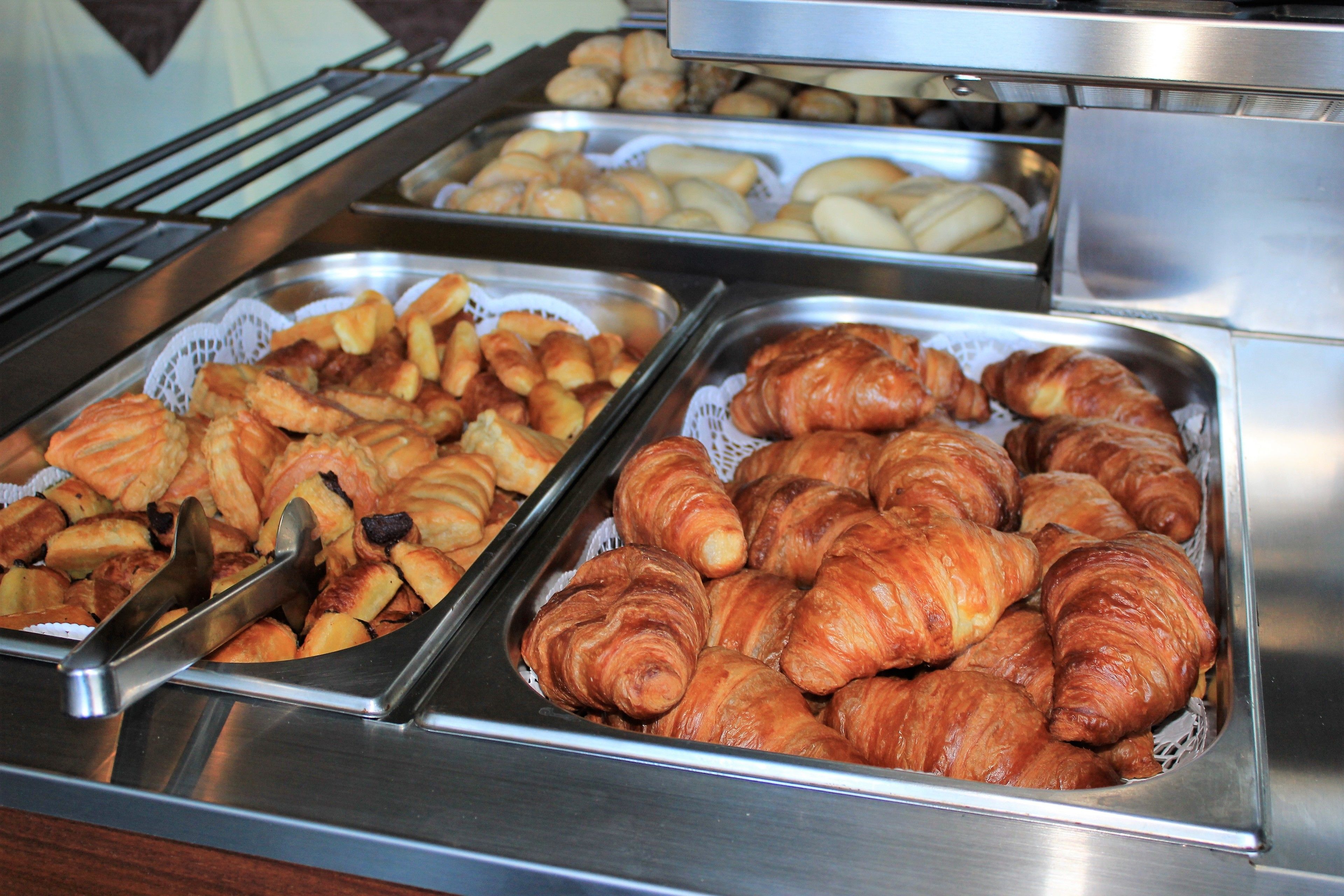 A buffet with trays of pastries including croissants and other baked goods.