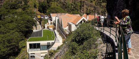 A modern building with a green roof, a staircase leading to a balcony, and a view of a valley.