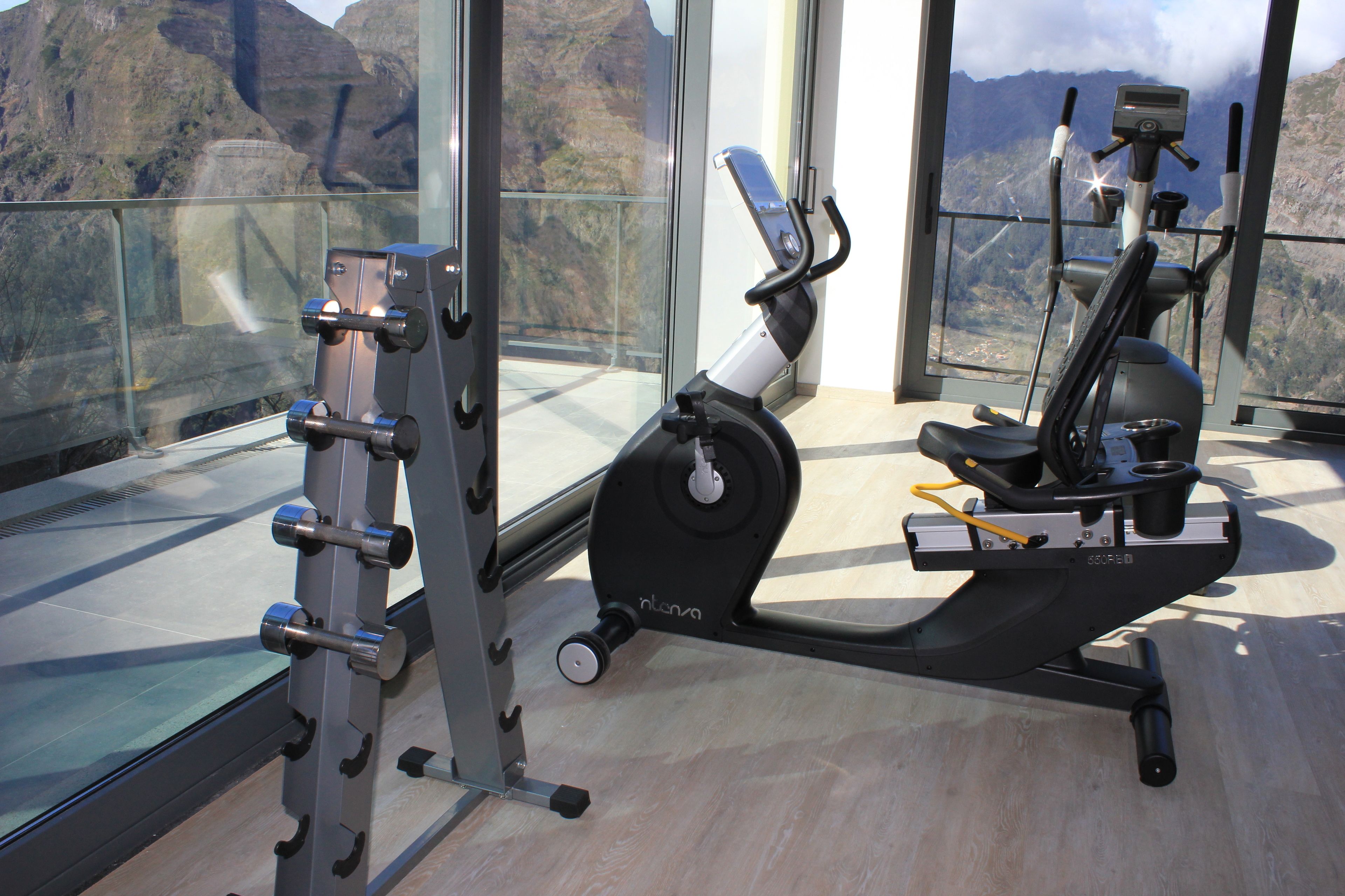 Un gimnasio con equipo de ejercicio, un muro de cristal y vistas a montañas.