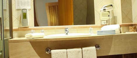 Baño con lavamanos, espejo e inodoro. Hay toallas colgadas en la pared y un secamanos en la encimera.