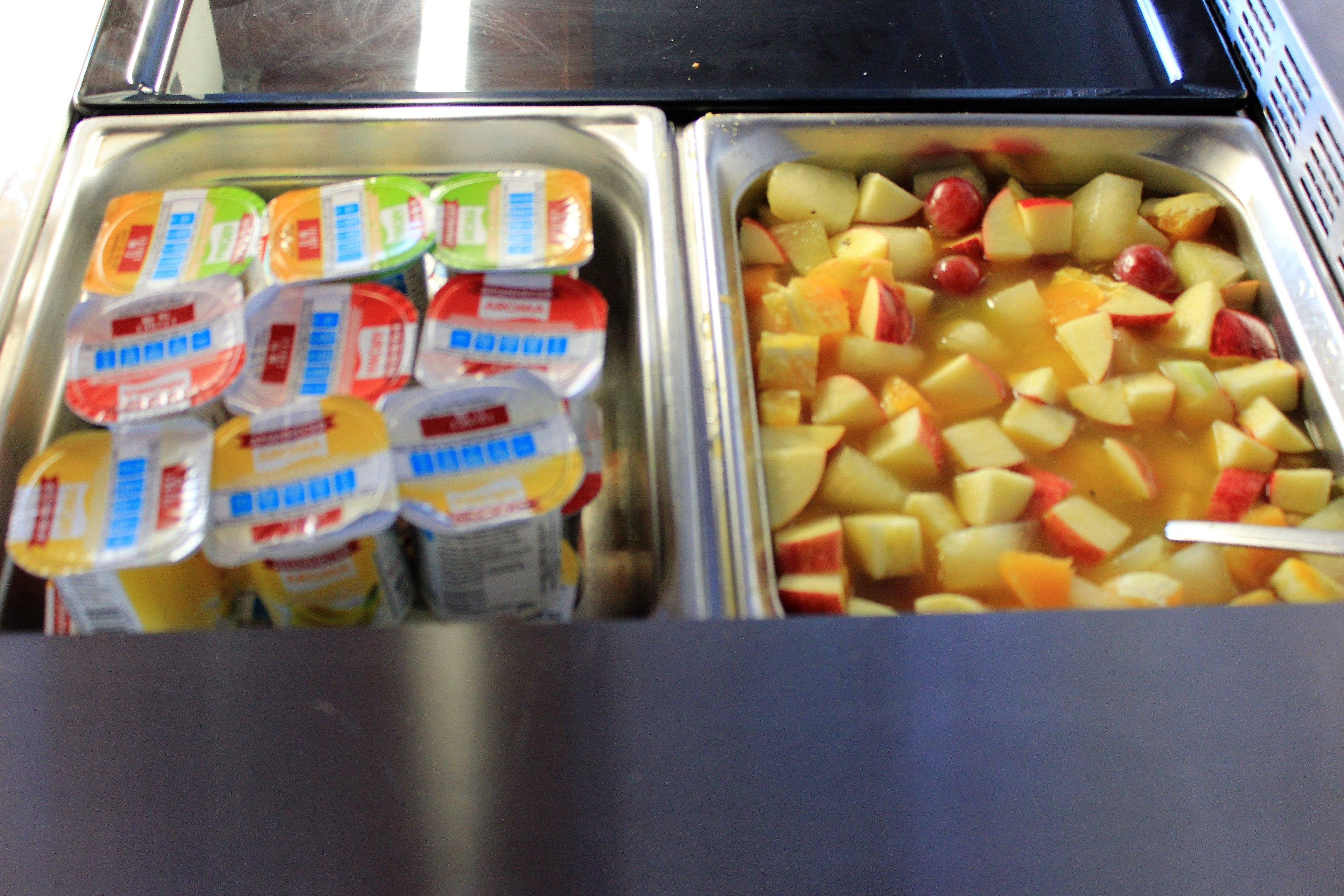 Un bufé con recipientes de yogur y fruta picada.
