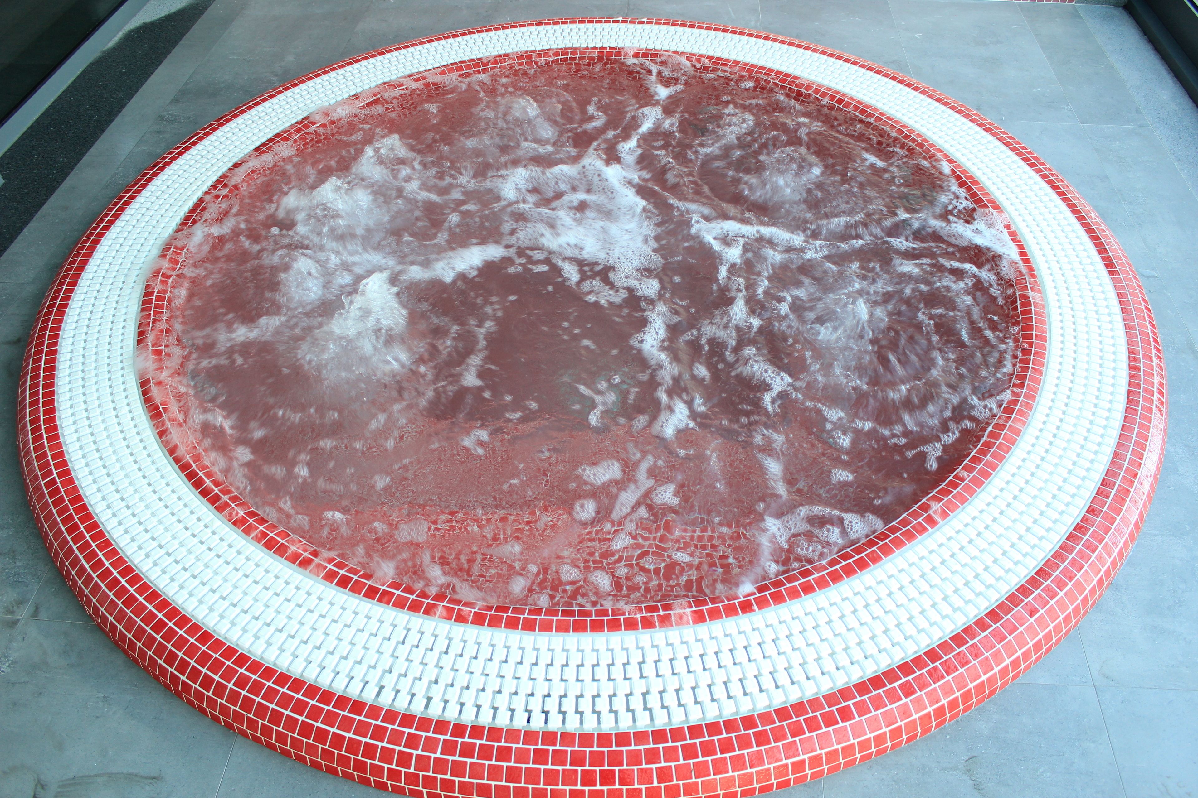 A circular hot tub with a red and white tiled border.
