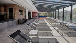 A modern hotel lobby with a glass ceiling, rows of lounge chairs, and a view of the mountains. - Eira do Serrado Hotel & SPA (Camara de Lobos)