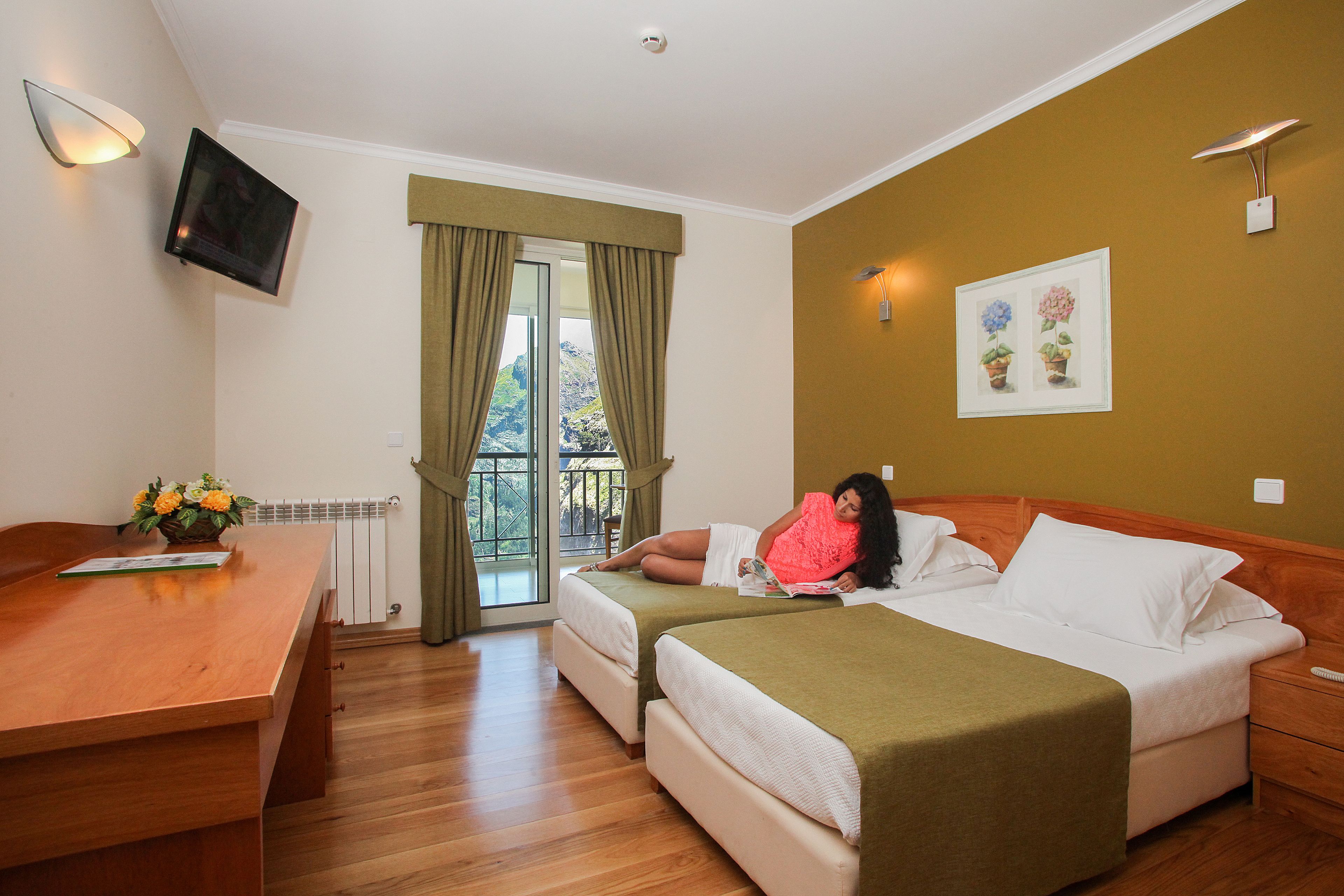 Habitación de hotel con dos camas, un escritorio de madera, un televisor montado en la pared y una ventana con cortinas.
