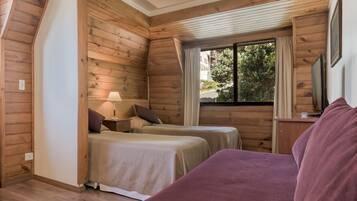 Een gezellig kamer in chaletstijl met twee bedden, een houten plafond, een raam met gordijnen en een televisie op een houten tafel.