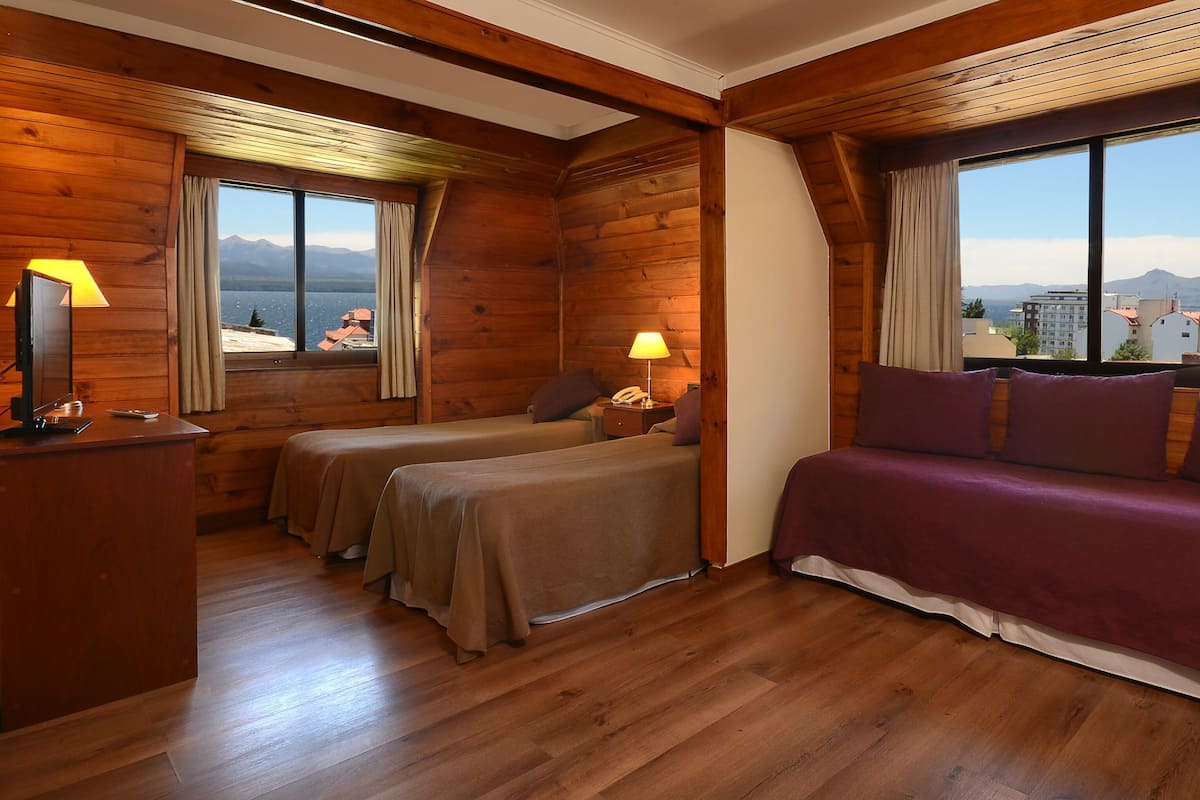 A wooden cabin room with two beds, a sofa, a desk, and a lamp.