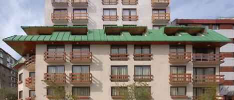 Ein mehrstöckiges Hotel mit Balkonen, einem begrünten Dach und mehreren Autos vor der Fassade.