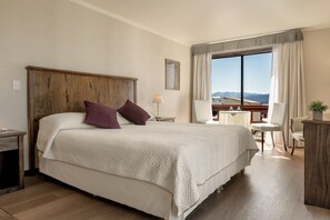 A hotel room with a large bed, a desk, a chair, a lamp, and a view of the mountains. - Soft Bariloche Hotel (San Carlos de Bariloche)