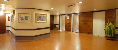 A hotel lobby with wooden flooring, framed artwork on the walls, and a potted plant.