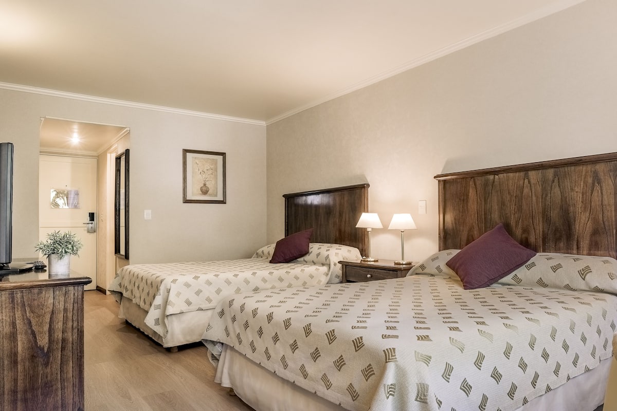 A hotel room with two beds, a wooden dresser, a desk, and a potted plant.