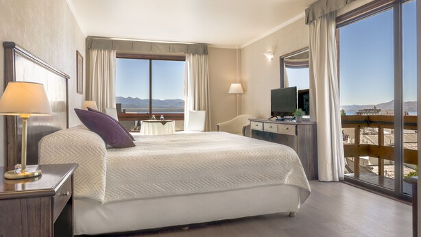 Habitación de hotel con una cama grande, un escritorio con una computadora, un televisor y vistas a la montaña.