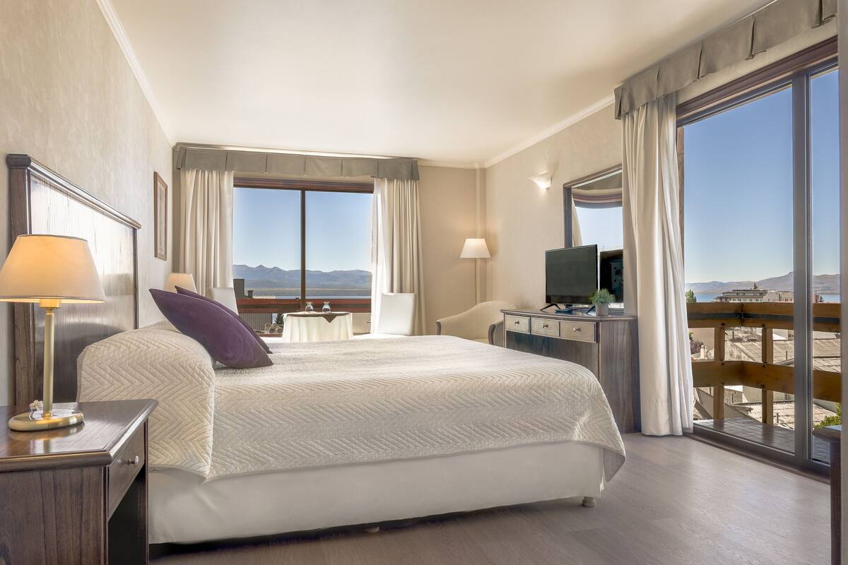 A hotel room with a large bed, a desk with a computer, a TV, and a view of the mountains.