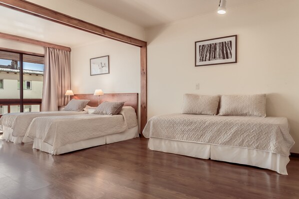 Habitación de hotel con dos camas, suelo de madera, un ventanal con cortinas y un cuadro en la pared.