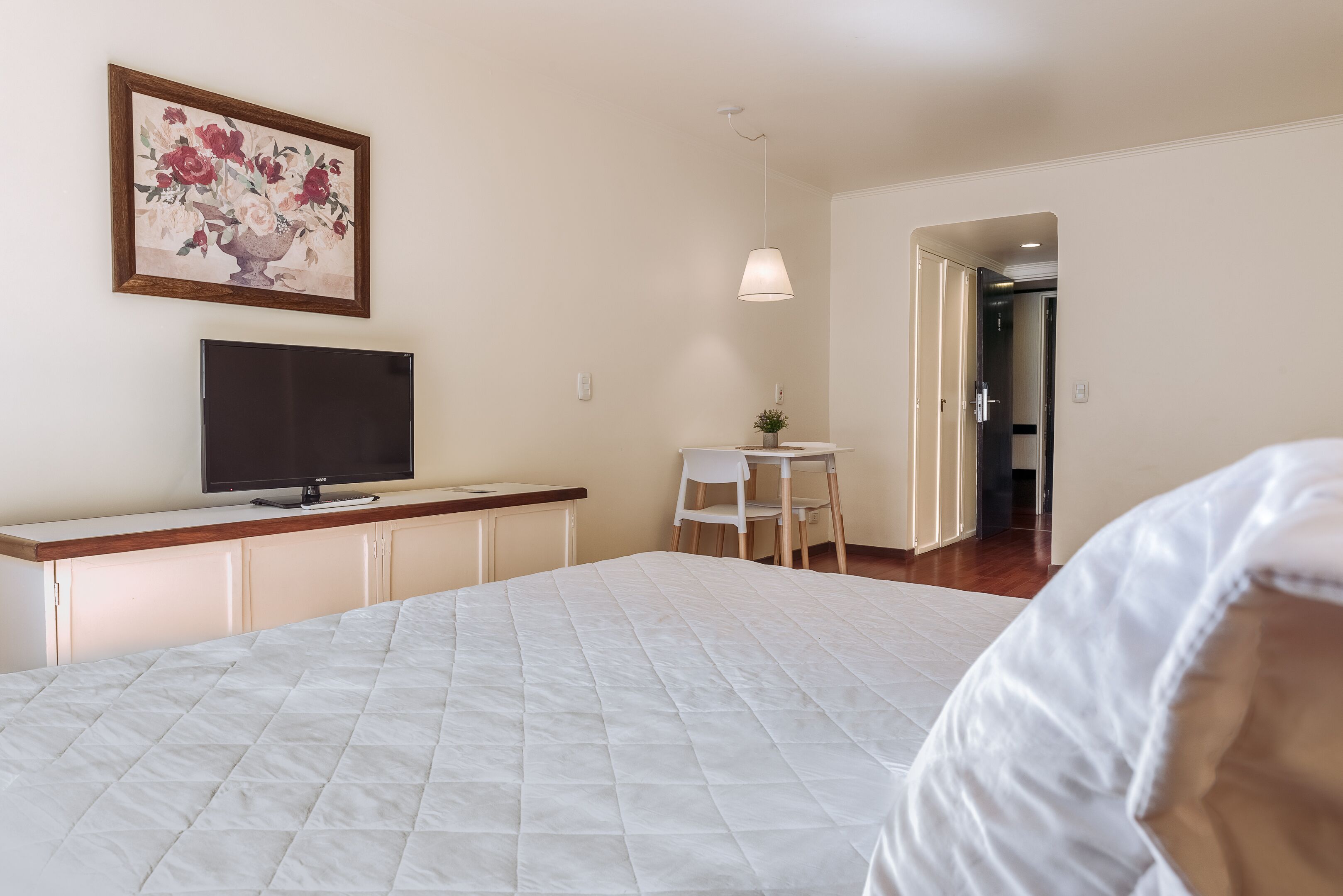 Une chambre d’hôtel avec un lit, un bureau avec une télévision, une chaise et une porte donnant sur une autre pièce.