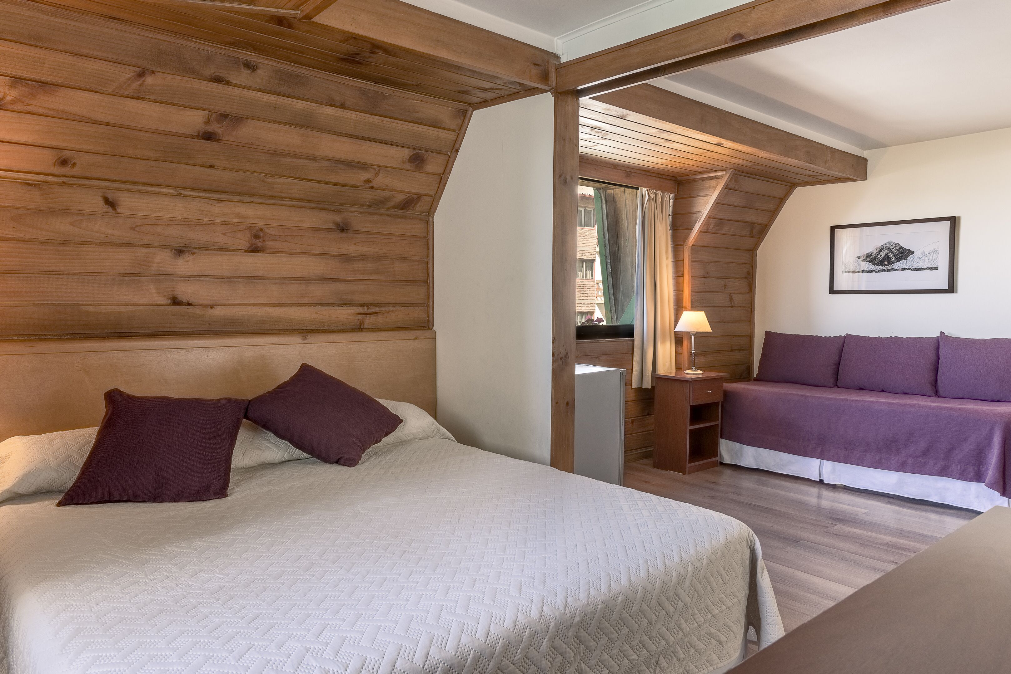 Un dormitorio con cama, mesita de noche, lámpara y sofá.