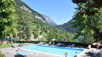 A pool area with lounge chairs and umbrellas, surrounded by lush greenery and mountains.