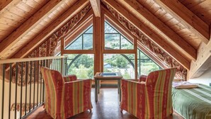 Una stanza mansardata con travi in legno, ampie finestre e vista sul verde.
