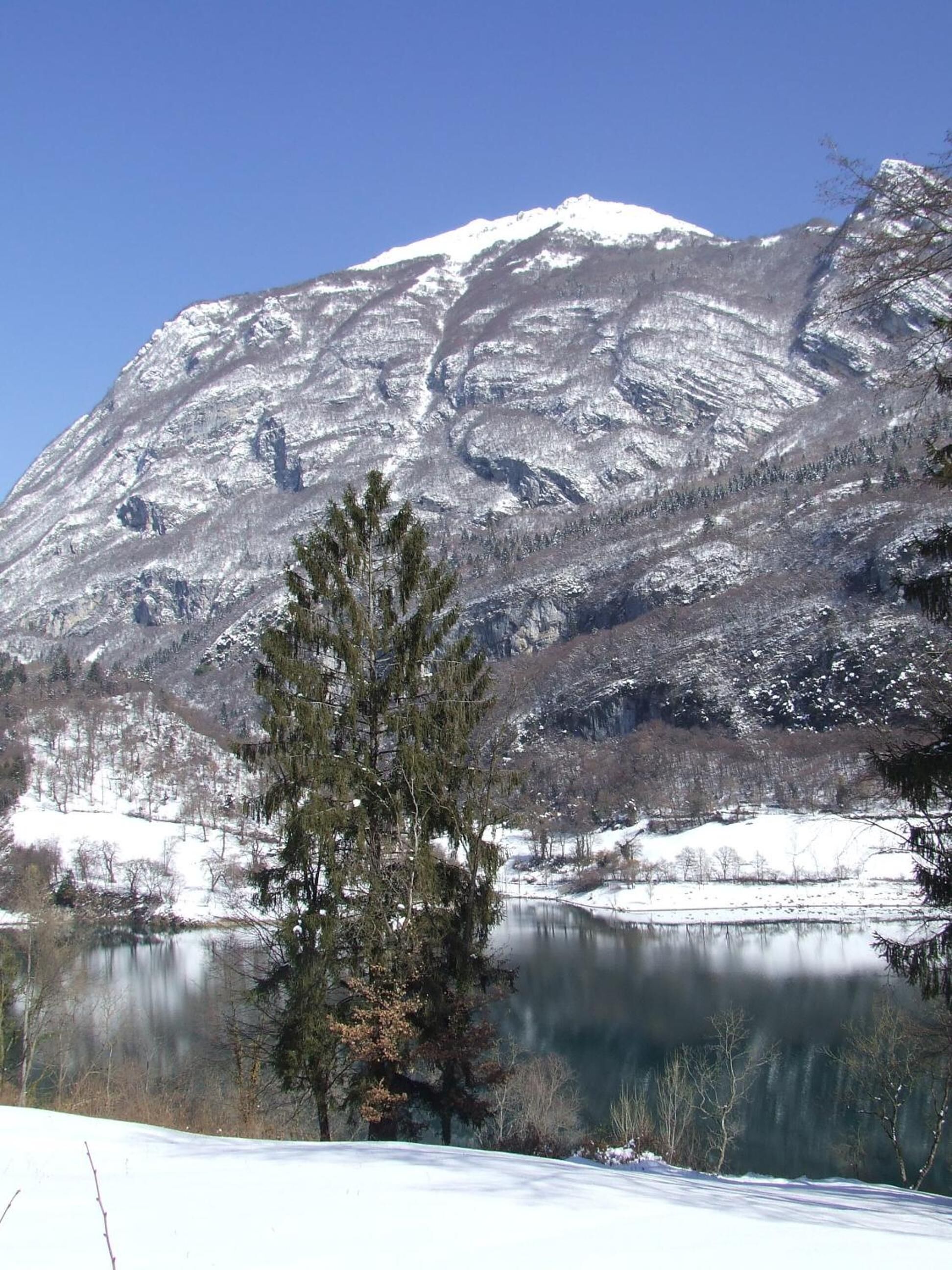 Una montaña con laderas nevadas y un lago en primer plano.