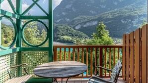 Un balcone con tavolo e sedie in legno, affacciato su un paesaggio montuoso con vista chiara sulla valle e un corpo d'acqua.